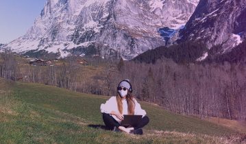 A girl sitting outdoors with a laptop on her lapa and headphones