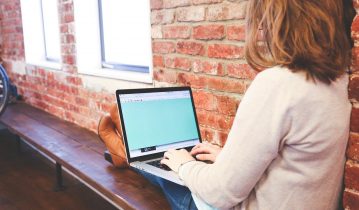 Woman typing on a laptop sating near to a window